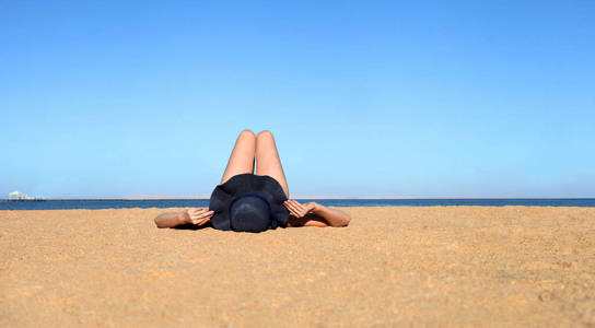 放松的假期。戴着帽子的女人在沙滩上放松，晒着太阳，在阳光明媚的夏日享受阳光。