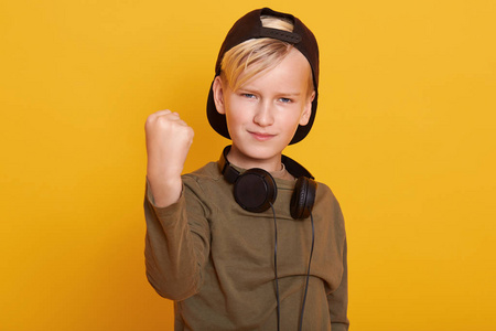 照片中的金发小男孩双手握拳,庆祝胜利或成功,看着摄像机,穿着毛衣和