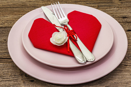 浪漫的餐桌，有盘子和心形餐巾。情人节或母亲节的爱情概念，婚礼餐具。复古木板背景