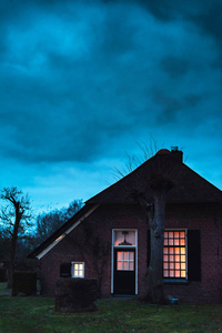 在暮色中,在暴风雨的天空下,有着发光窗户的令人毛骨悚然的房子照片