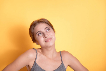 一个穿着灰色T恤的年轻漂亮女孩在瘦弱的英国，一个快乐的金发模特在黄色的墙上带着雪白的微笑微笑。