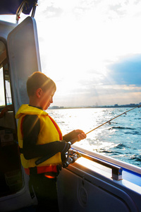 日落时小男孩在船上用鱼竿钓鱼图片