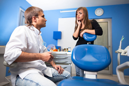年轻的女病人站在牙医椅旁，向年轻的牙医医生展示牙科诊所的坏牙