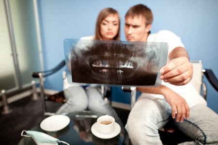 一对年轻夫妇坐在牙科诊所里，看着牙科照片，喝着茶