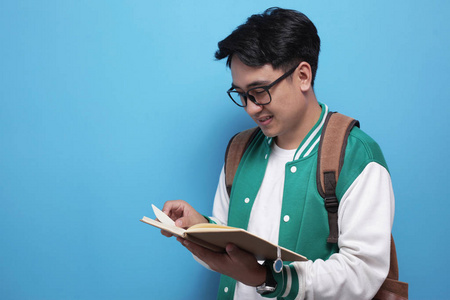 男亚裔学生在蓝色背景下微笑着看书照片