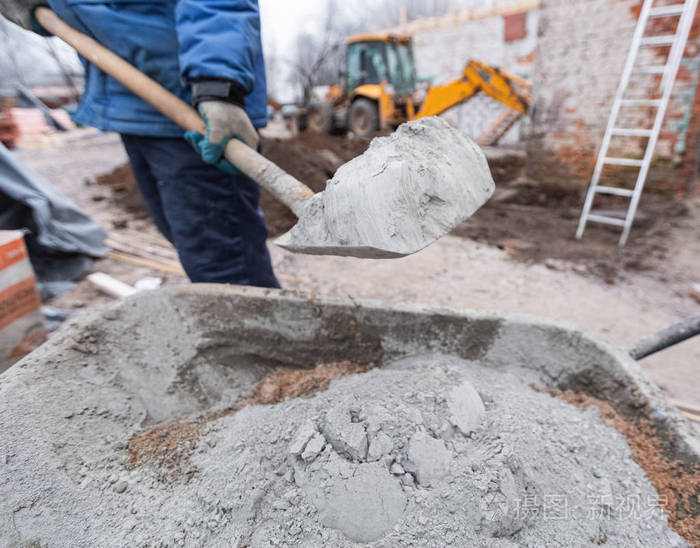 施工现场戴防护手套的工人正在用铁锹将水泥装载到装有沙子的建筑台车