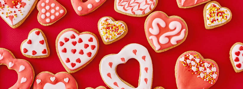 背景用糖霜和釉面的心形饼干装饰在红色的背景上，长长的横幅。情人节美食概念