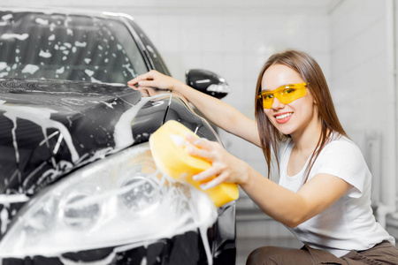 工人美女用黄色海绵清洗汽车黑色泡沫。洗车服务