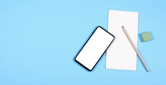 一部现代智能手机躺在一个纸质记事本上，旁边是铅笔和橡皮擦。蓝色背景。