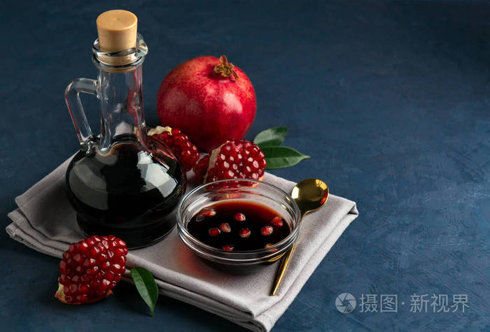 石榴酱在一个瓶子和碗与谷物和石榴块在深蓝色的背景
