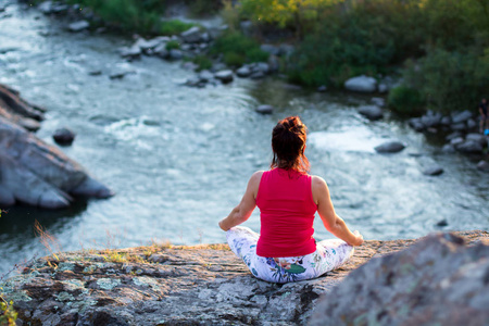 日落时在白水河上的岩石上做瑜伽体式的成年妇女