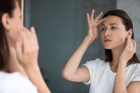 焦急的女人照镜子,摸摸额头,迷茫于皱纹照片