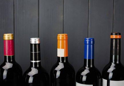 Red wine bottlenecks labeled of different colors on gray wooden 