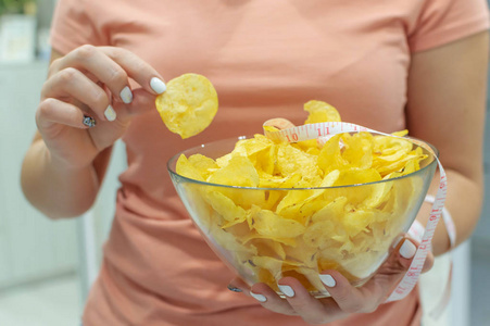 女孩手里拿着一盘薯片和一厘米长的胶带.垃圾食品.