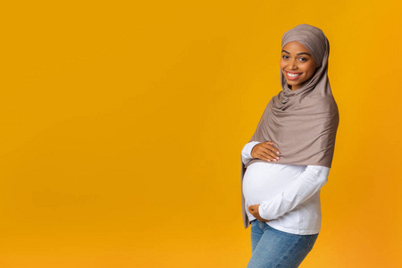 怀孕的非洲穆斯林妇女的头巾拥抱她的腹部肖像