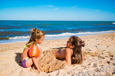 快乐的小女孩把姐姐埋在沙子里