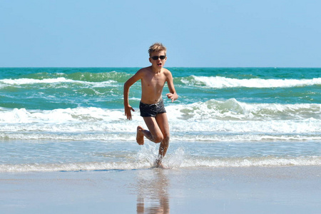 小男孩跑出了大海。快乐的孩子在海滩上奔跑。