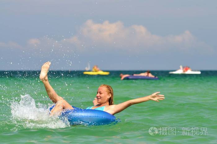 年轻的金发女子穿着蓝色比基尼骑在游泳圈里面带微笑