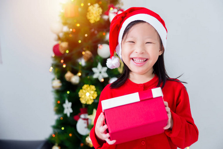 亚洲小女孩戴着圣诞老人的帽子，手里拿着礼品盒，笑容满面
