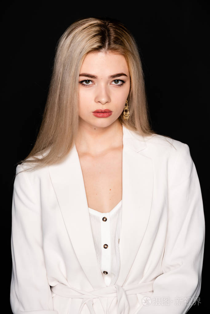 一个金发黑衣的年轻漂亮模特的特写在摄影棚里摆出一副黑色的背景