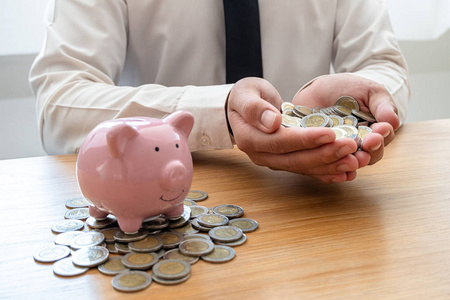 一个拿着硬币的商人的手放在存钱罐旁边以存钱，发展成功的企业，为退休储蓄