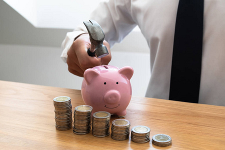 商人用锤子藏着粉红色的小猪存钱罐和硬币堆，逐步发展壮大的企业，以成功和为退休储蓄的理念
