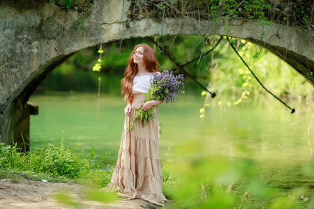 一个穿着长裙的女人走在河上那座古老的森林桥附近