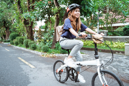 一位亚洲年轻女子戴着头盔和一个包骑着她的折叠自行车