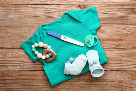 怀孕测试，婴儿衣服和玩具在木制背景上