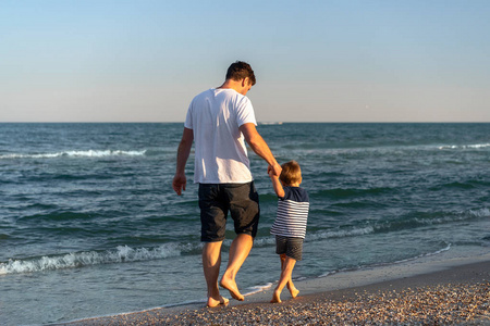 Young Caucasian dad with little son walk warm summer day along t