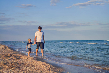 Young Caucasian dad with little son walk warm summer day along t