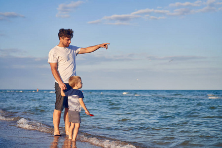 Young Caucasian dad with little son walk warm summer day along t