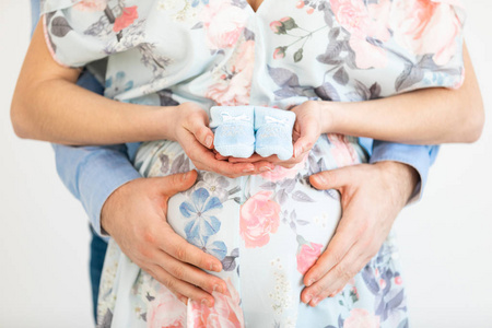 Young pregnant woman holds baby booties in front of her belly  