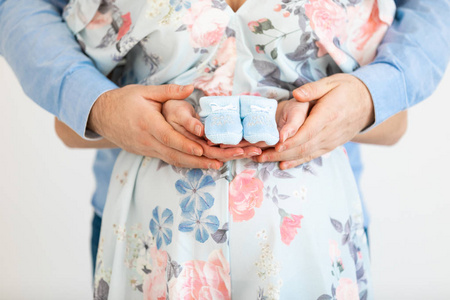 Young pregnant woman holds baby booties in front of her belly  