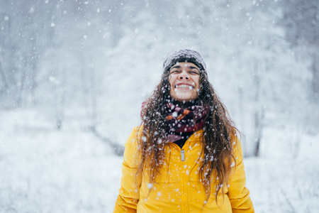 穿着黄色夹克的快乐女孩在冬天的森林里扔雪。