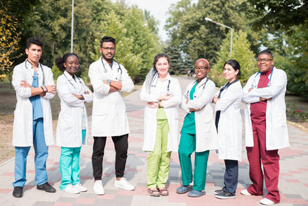 混血医生团队。一群穿着彩色医疗服的不同性别的年轻人，站在街上，站在街上，拿着电话内视镜，摆姿势，微笑着
