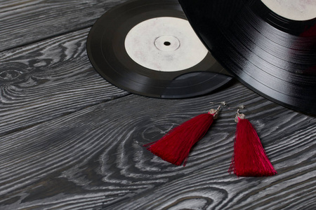 自制红色流苏耳环。以旧的乙烯基唱片和黑白相间的拉丝松木板为背景。