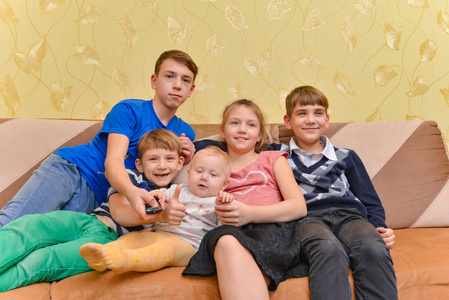 快乐快乐的孩子们坐在客厅的沙发上。男孩打开电视遥控器切换频道
