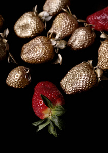 黑色背景上是红色和金色的草莓.金色的水果.垂直构图,平铺.照片