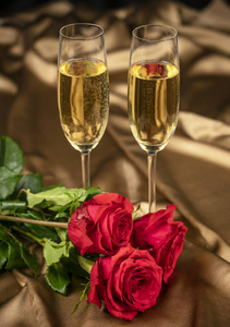 红玫瑰和两杯香槟在金色锦缎的背景上，以纪念情人节结婚纪念日