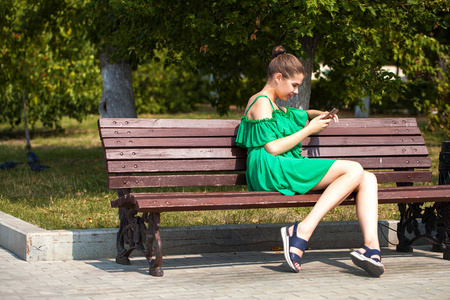 Sexy beautiful caucasian girl in green dress sitting on a bench 