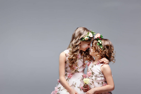 亲子拥抱两个可爱的小女孩姐妹头戴鲜花,坐在明亮的工作室里拥抱.