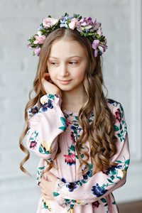 一个美丽可爱的小女孩在一个明亮的工作室里,头上戴着一圈鲜花,摆出