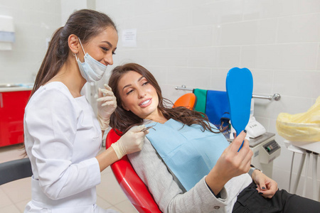 牙医。牙医办公室的一位女士对着镜子检查自己的牙齿，微笑着。