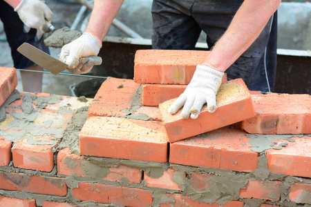 Bricklayer hands in masonry gloves and trowels bricklaying house