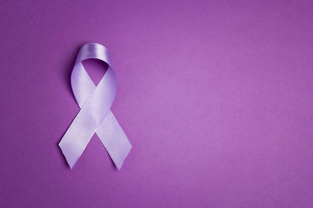 Purple awareness ribbon on a purple backgroundwith copy space. 