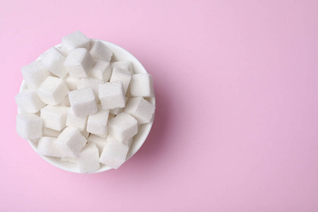 Refined sugar cubes in bowl on pink background, top view. Space 