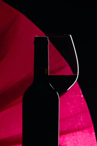 Closed bottle and glass of red wine on a black background. Copy 