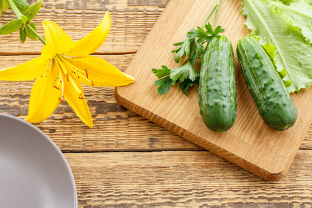 刚摘下的黄瓜和沙拉叶放在菜板上，上面有花和盘子。