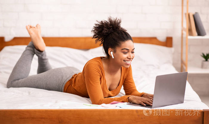 非洲裔美国女孩躺在床上用笔记本电脑在线学习